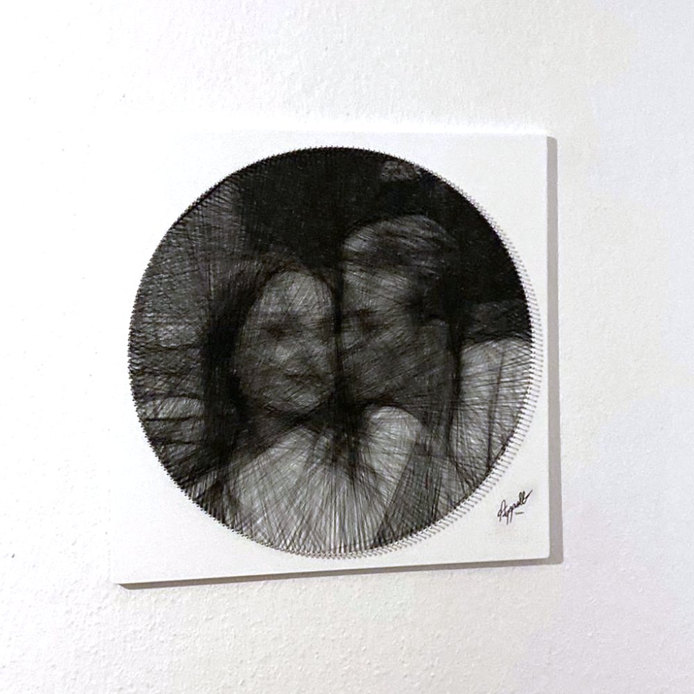 Echtes Fadenbild an einer weißen Wand: Paarporträt aus schwarzem Faden auf weißem Brett, unten rechts signiert